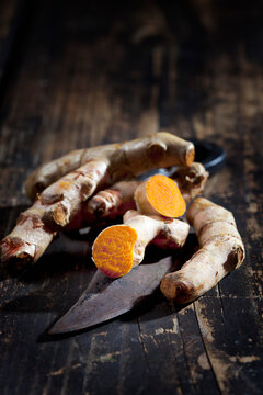 Whole and sliced turmeric and an old knife on dark wood