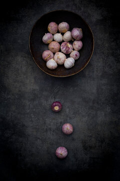 Fresh single clove garlic rests in a bowl on dark concrete