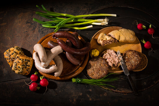 Liver sausage, blood sausage,  spring onion, red radish, chives, mustard, bread on chopping board, hotplate