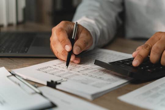 Businessman pointing at printed financial documents with pen while using calculator for corporate budgeting, accounting review, revenue analysis, expense control, strategic budget planning.