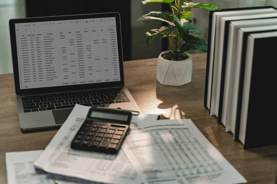 Laptop spreadsheet with calculator and financial reports on office desk for invoice review, receipt accounting, cash flow monitoring, bookkeeping, finance reporting.