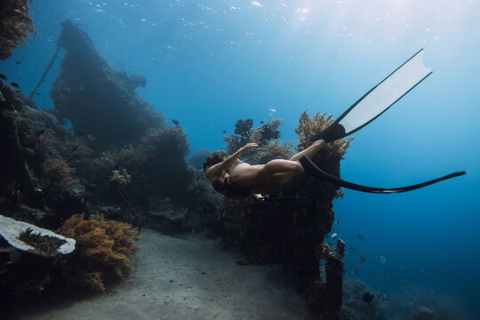 Woman free diving near coral reef underwater, marine life and wreck in clear ocean