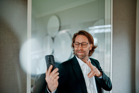 Smiling businessman greets someone during a smartphone video call