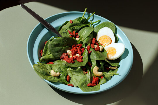 A blue bowl contains a healthy spinach salad with egg and goji berry
