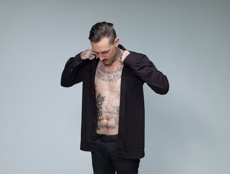 Man with tattoo on his waist up dressing black shirt in front of grey background