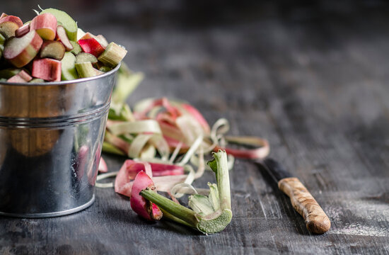 Rhubarb pieces in bucket with rhubarb cuttings and knife on wooden table, close up