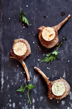 Three differently flavoured compound butters on lamb chops and parsley leaves on slate