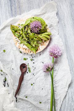 Rice cakes with cream cheese, avocado and asparagus garnished with black cumin seeds and chive blossom
