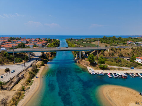 Aerial view of Nea Potidea Beach canal with a bridge crossing over turquoise waters, small boats docked at the pier, and surrounding coastal landscape in Greece.