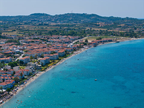 Aerial view of Skala Fourkas Beach with its turquoise waters, sandy shoreline, and surrounding residential buildings in Halkidiki, Greece.