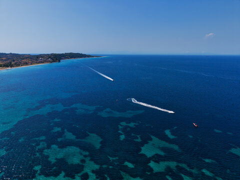 Aerial view of Skala Fourkas Beach with boats and jet skis leaving wakes on the clear turquoise and deep blue sea off the coast of Halkidiki, Greece.