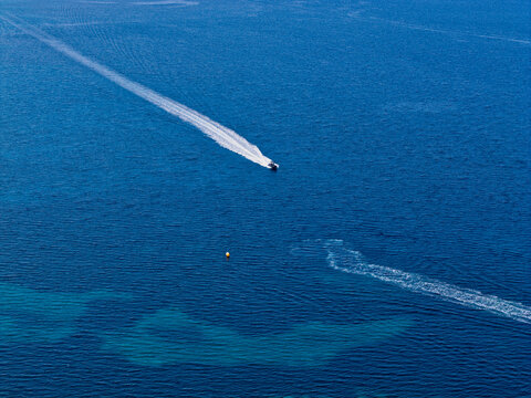 Aerial view of a small motorboat leaving a white wake on the deep blue waters of the Aegean Sea near Skala Fourkas Beach in Halkidiki, Greece.