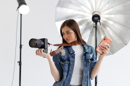 Smiling beautiful woman photographer holding manual camera and use phone while sitting at her working place.