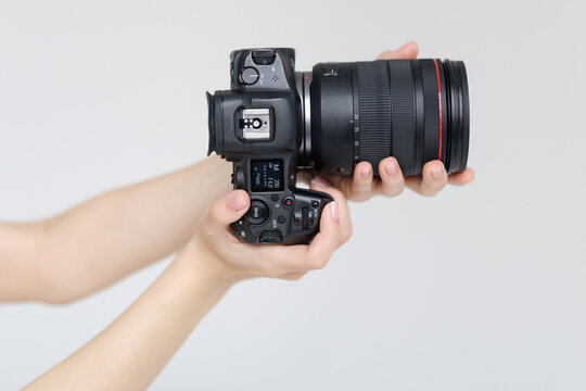 Human hand firmly holds professional camera with lens hood pointing forward on white background