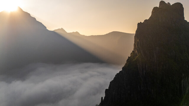 Aerial view of Gunung Kelud at sunrise with dramatic light rays piercing through the clouds over the volcanic peaks in Kecamatan Ngancar, Jawa Timur, Indonesia.