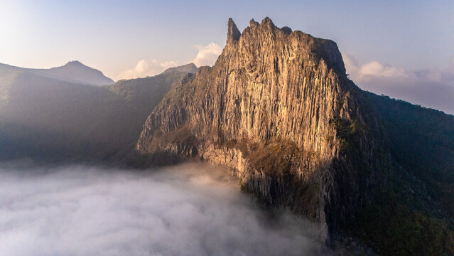Aerial view of Gunung Kelud rising above a thick layer of clouds during golden hour in Kecamatan Ngancar, Jawa Timur, Indonesia.