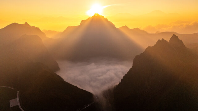 Aerial view of Gunung Kelud at sunrise with golden light illuminating the mountain peak and a sea of clouds filling the crater in Kecamatan Ngancar, Jawa Timur, Indonesia.