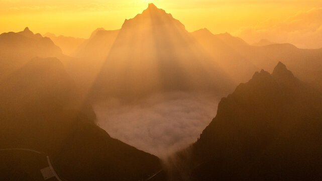 Aerial view of Gunung Kelud at sunrise with golden light rays and a sea of clouds filling the volcanic crater in Kecamatan Ngancar, Jawa Timur, Indonesia.