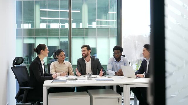 Team businesspeople communicate at meeting sitting in conference room in modern business office. Group multiethnic co-workers talking, discussing work issues in positive atmosphere, engaging teamwork