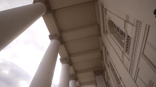 Low-angle upward view of classical colonnade with tall Corinthian columns under overcast sky, with architecture, column, colonnade, corinthian detail, showing capital, entablature, soffit, coffer