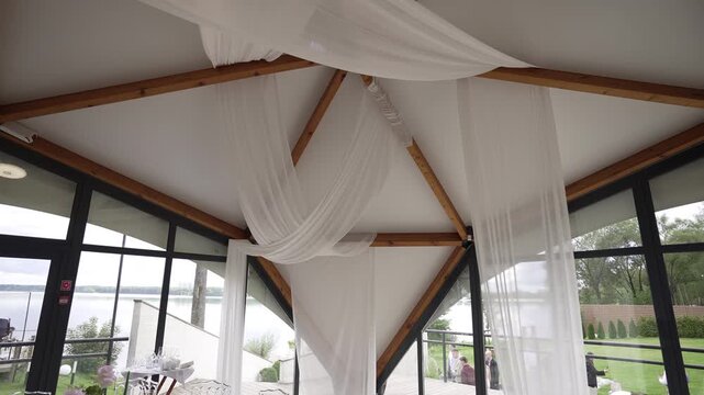 Sheer drapery settling over exposed timber trusses in lakeside event pavilion, with drapery, fabric, interior, pavilion detail, showing truss, beam, timber, ceiling