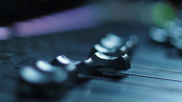 Close up shot of audio faders on a professional sound mixing console in a recording studio. Automated controls move smoothly during music mixing and post production mastering