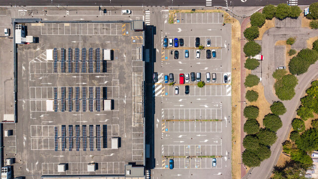 Aerial view of the Pittarello building featuring extensive rooftop solar panels and an adjacent parking lot with parked cars in Peschiera Borromeo, Lombardia, Italy.