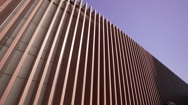 Low-angle overview of exterior facade with repeating vertical wooden fins and diagonal perspective toward sky, with architecture, facade, wood, louver detail, showing fin, panel, repetition, pattern
