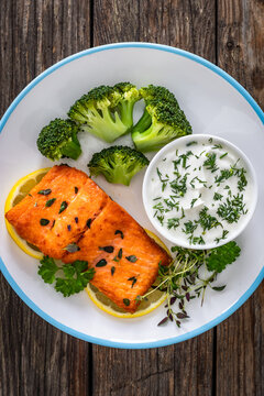 Fried salmon steak with boiled broccoli and dill yogurt sauce on wooden table. Top view
