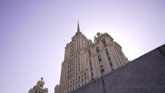 Low-angle ornate high-rise with rising spire under pastel lavender sky showing increasing backlight, with building, architecture, highrise, facade detail, showing spire, ornament, stone,pilaster
