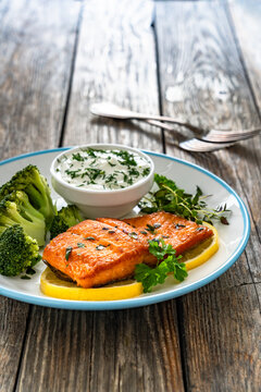 Fried salmon steak with boiled broccoli and dill yogurt sauce on wooden table

