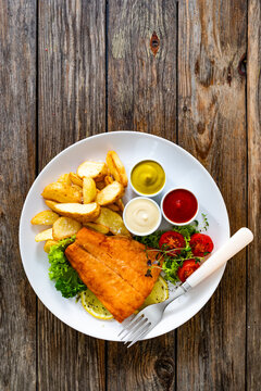 Fried salmon fillet with fried potato wedges, fresh salad and mayonnaise, ketchup, mustard on wooden table. Top view

