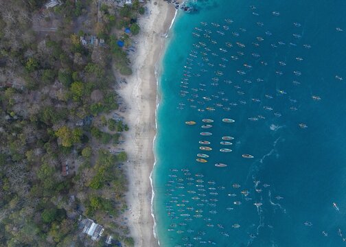 Aerial view of Papuma Beach featuring numerous traditional fishing boats anchored in the turquoise waters along the sandy coastline in Jember, East Java, Indonesia.