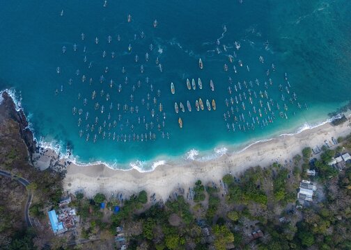 Aerial view of Papuma Beach with numerous traditional fishing boats floating in the turquoise water along the sandy coastline in Jember, East Java, Indonesia.