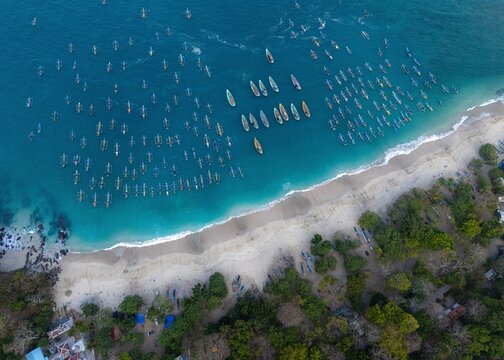 Aerial view of Papuma Beach with numerous traditional fishing boats anchored in turquoise waters along the sandy coastline in Jember, East Java, Indonesia.