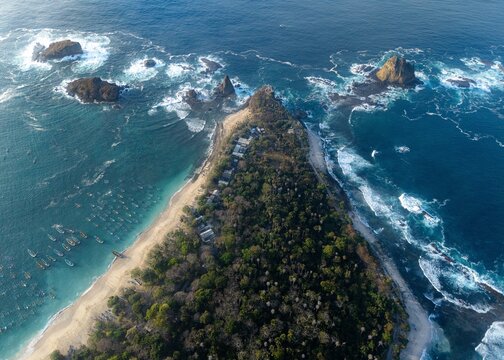 Aerial view of Papuma Beach featuring lush tropical forest, sandy coastline, turquoise ocean waters, and traditional fishing boats anchored in Jember, East Java, Indonesia.