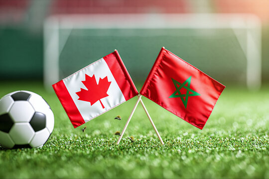 Canada and Morocco flags placed on green soccer field grass with a football. Perfect for international sports tournament and match preview concepts.