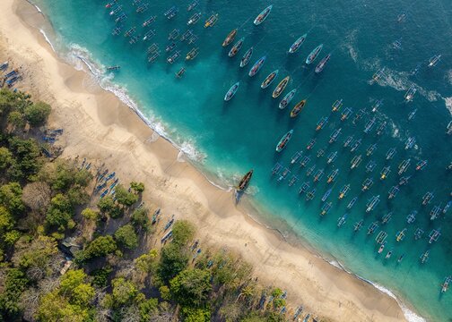Aerial view of Papuma Beach featuring numerous traditional fishing boats anchored in the turquoise waters along the sandy coastline in Jember, East Java, Indonesia.