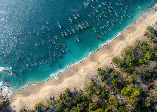 Aerial view of Papuma Beach with numerous traditional fishing boats anchored in the turquoise waters along the sandy coastline and lush green trees Jember, East Java, Indonesia.