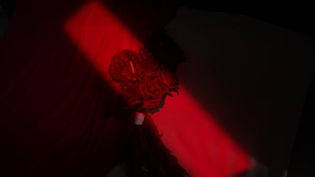 Red spotlight revealing bouquet of roses over draped background, narrow beam across dark space gradually exposing lower petals, wrapped stem, rich texture dramatic contrast