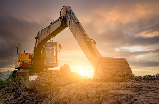 Backhoe parked at construction site after digging soil. Bulldozer on sunset sky and clouds background. Digger after work. Earth moving machine at construction site at dusk. Digger with dirt bucket.
