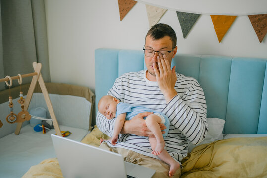 Tired father working from home with sleeping newborn, experiencing parental burnout and balancing new dad duties with remote work challenges
