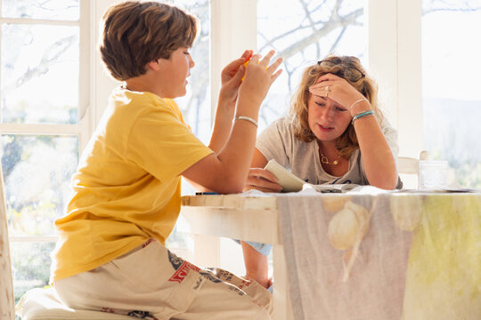 13 year old boy doing homework with older sister looking on in light filled room