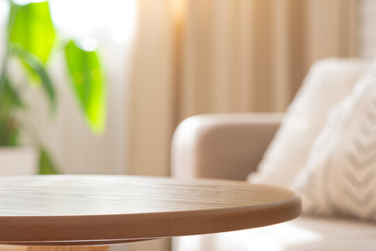 Round wooden empty table top in daylight on blurry living room interior background