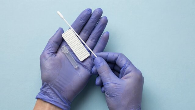 Medical professional holding a rapid antigen test kit and nasal swab for health screening.