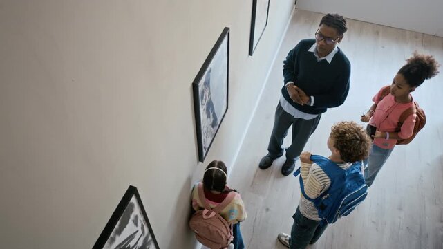 African American male guide explaining art to multiethnic school children in gallery, high angle view. Clip perfect for educational marketing, museum ads, and school field trip promotions