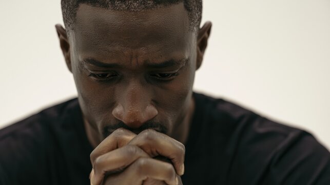 Man with hands clasped together looks down in thought indoors