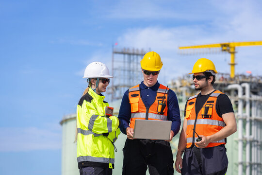 LNG plant engineers team with laptop working outdoors at storage terminal facility, Liquefied natural gas plant workers discussing project with laptop at industrial site