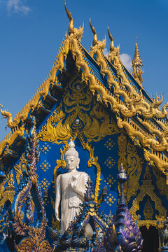 Standing White Buddha Statue and Ornate Blue and Gold Gable at Wat Rong Suea Ten Blue Temple in Chiang Rai Thailand