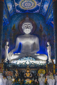 Giant White Seated Buddha Statue Surrounded by Intricate Blue Murals Inside Wat Rong Suea Ten Blue Temple in Chiang Rai Thailand
